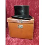 A black silk top hat in brown leather carrying case.