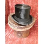 A black silk top hat in fitted brown leather carrying case.