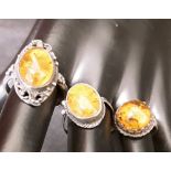 Three silver rings each with a large central amber stone.