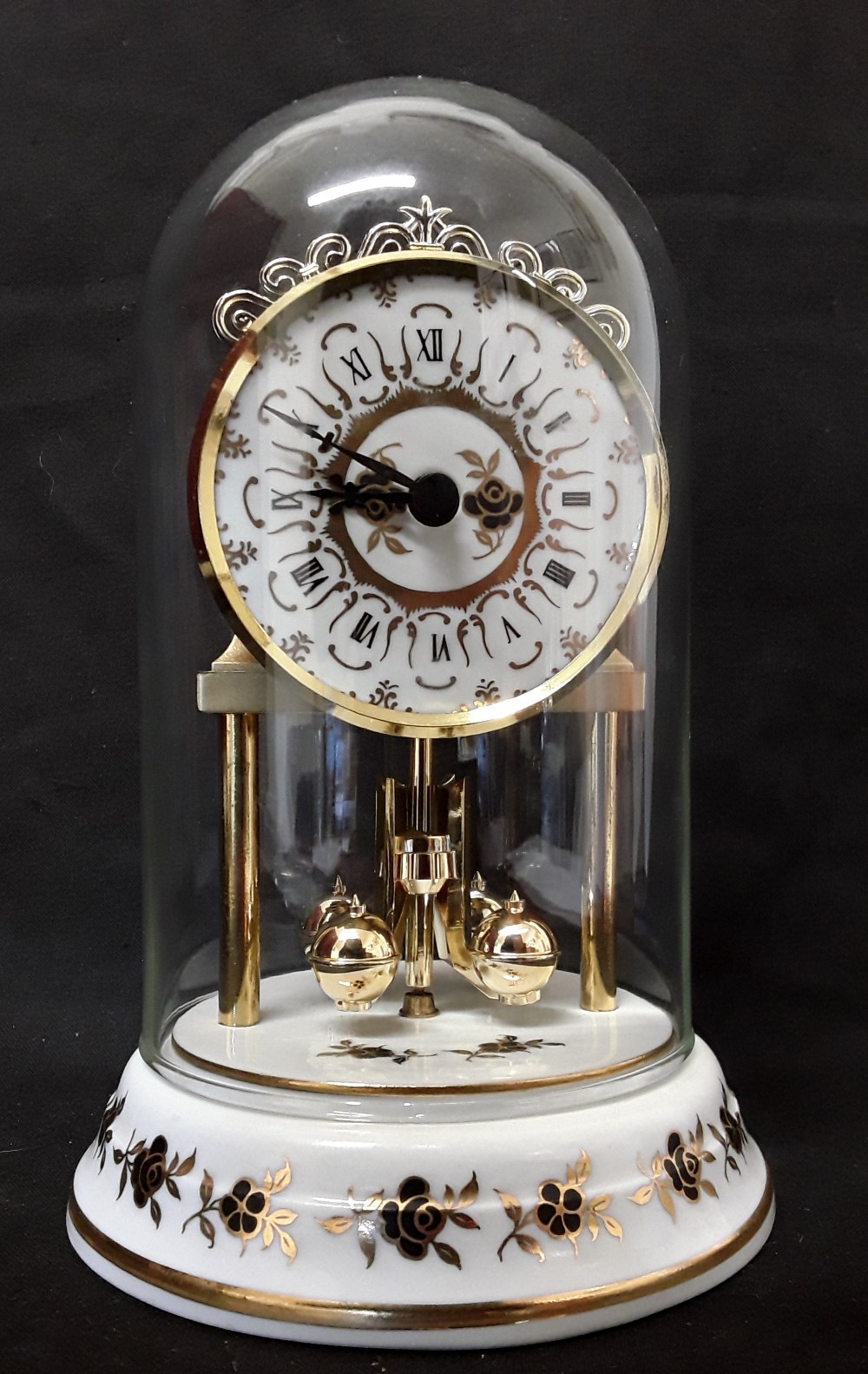 A domed revolving pendulum mantel clock with a porcelain base.