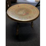 A brass table with a brightly coloured peacock as decoration to the circular top,