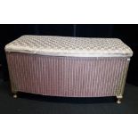 A Lloyd Loom ottoman in pink with cushioned seat and bowed front.