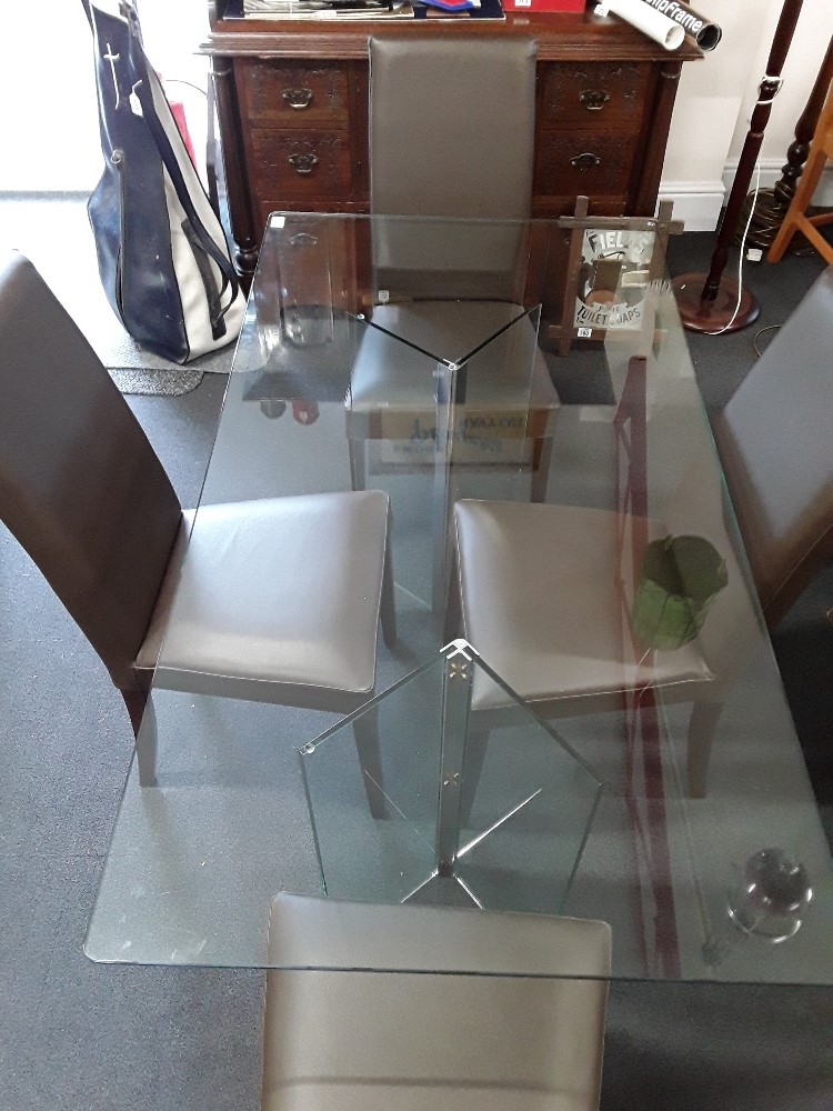 A contemporary four seater glass dining table together with four leather highbacked chairs.