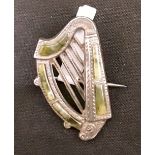 A white metal harp shaped booch set with green stone inlay.