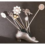 A white metal pincushion in the form of a shoe with eight gold and silver tie pins.