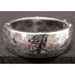 A large white metal bangle marked Hong Kong, with engraved decoration of flowers to the outside.