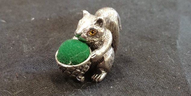 A silver pincushion in the form of a squirrel and a nut.