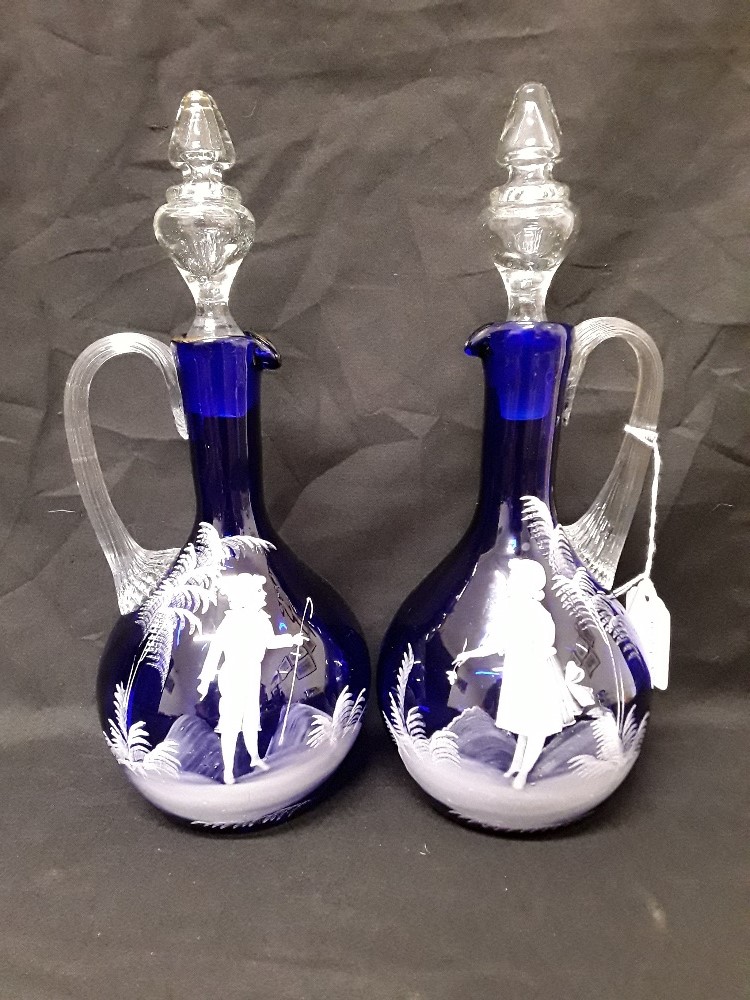 A pair of Mary Scott hand blown blue glass decanters/water jugs decorated with white enamel figures.