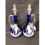 A pair of Mary Scott hand blown blue glass decanters/water jugs decorated with white enamel figures.
