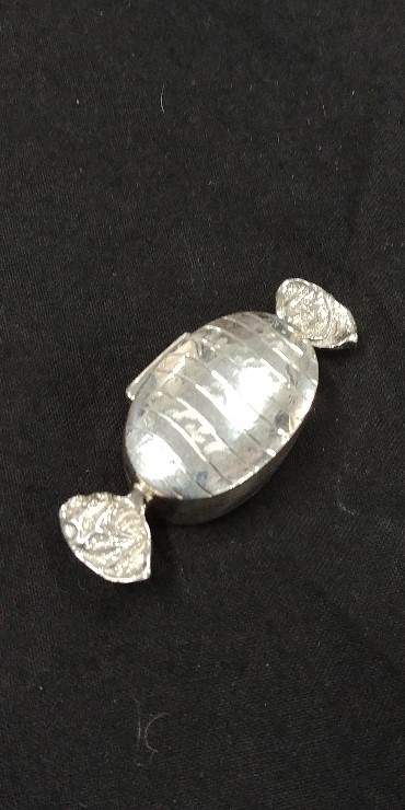 A silver pill pot in the form of a wrapped sweet.