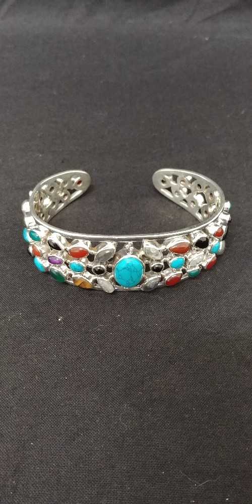 A large silver bangle set with a variety of stones