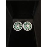 A pair of silver stud earrings set with CZs and emeralds.