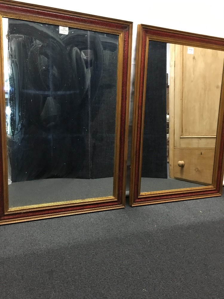 A pair of tall wall hanging mirrors with red leather frames edged in gold.