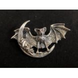 A silver brooch in the form of a bat set with ruby eyes and a half moon.