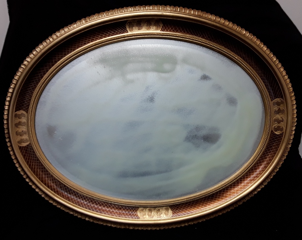 A large oval shaped mirror with bevelled edge to the glass enclosed in a gilded patterned frame.