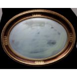 A large oval shaped mirror with bevelled edge to the glass enclosed in a gilded patterned frame.