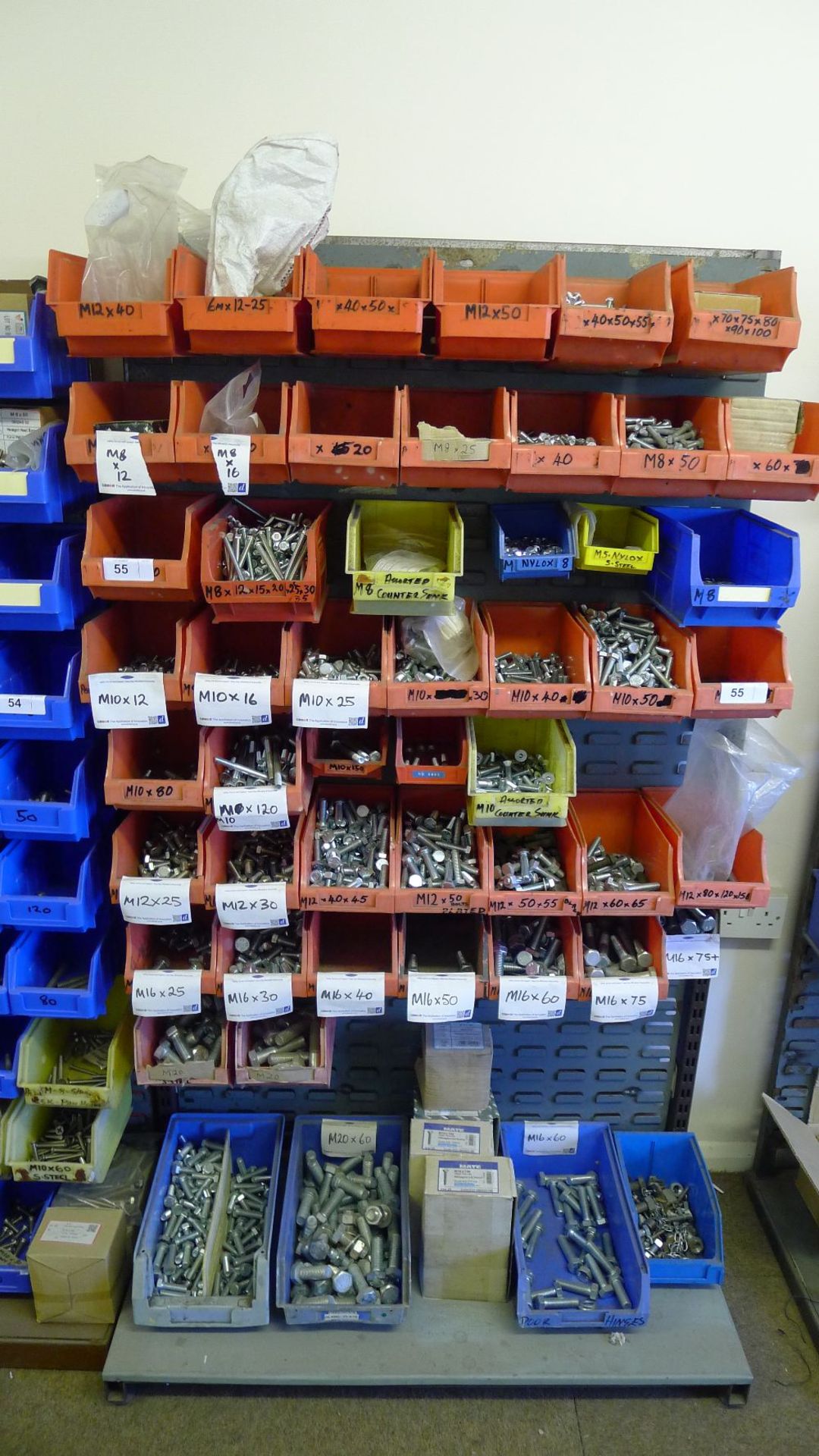 A quantity of plastic Lin type bins hanging on a free standing rack containing a large quantity of