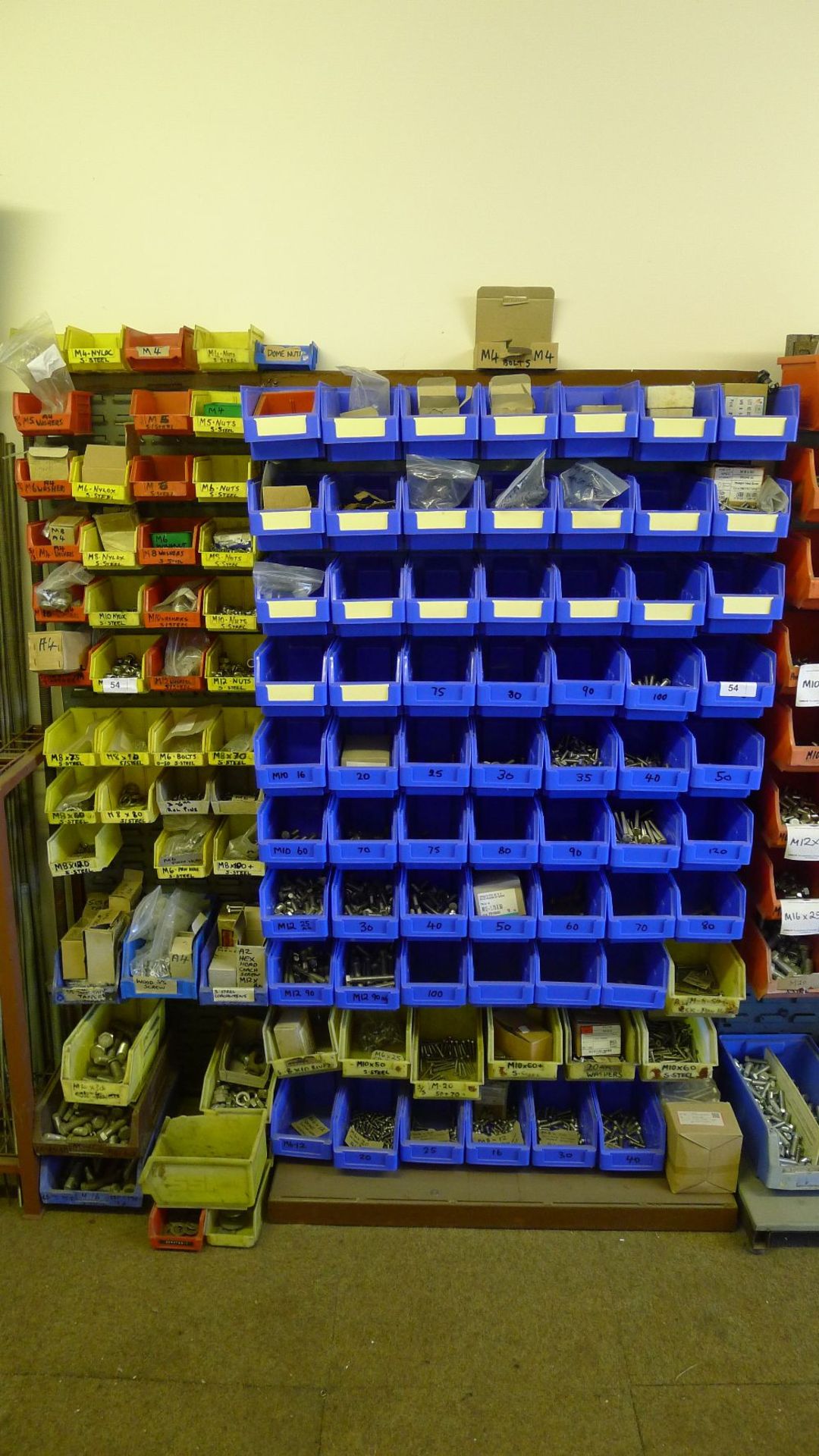 A quantity of plastic Lin type bins hanging on a free standing rack containing a large quantity of