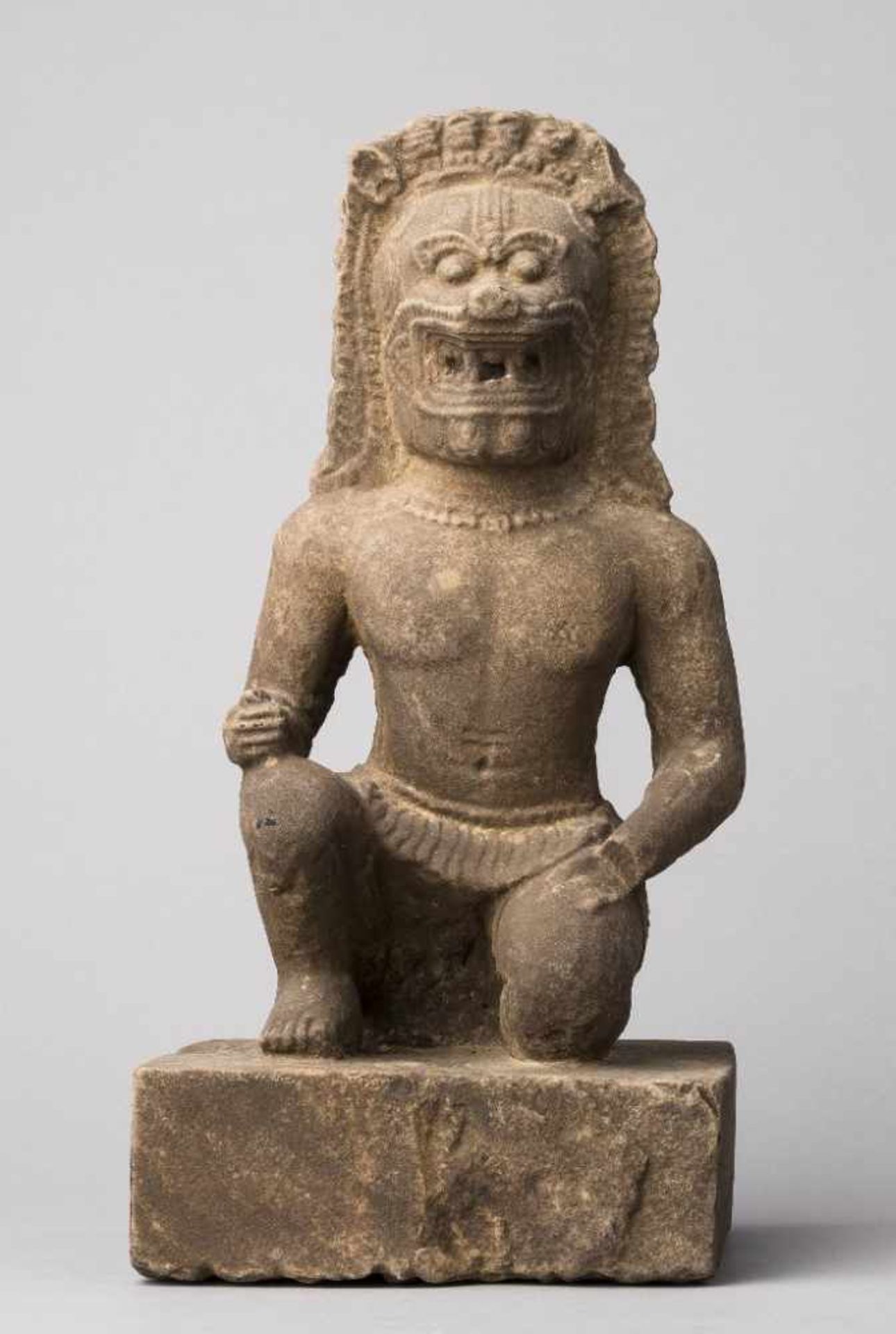 Wächterfigur mit Löwenhaupt, mit einem Bein auf quadratischem Plinthensockel kniend. Stein,