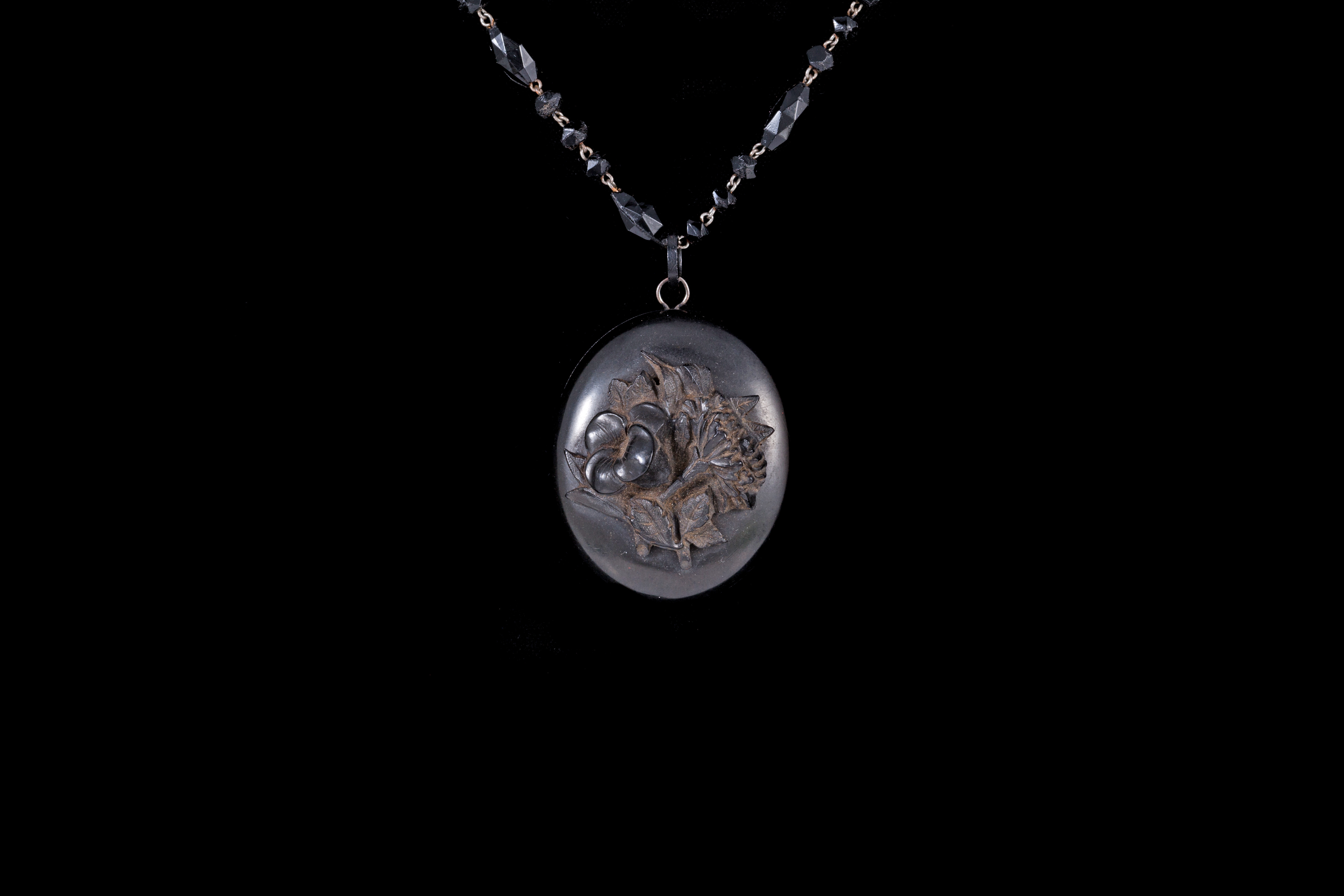 A JET LOCKET PENDANT, with intaglio motif interior, on black beaded chain