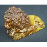 19TH CENTURY GLAZED POTTERY STUDY OF A RECUMBENT MALE LION on rectangular plinth.