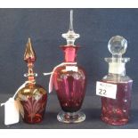 A group of three cranberry glass scent bottles of various designs with stoppers. (3) (B.P. 24% incl.