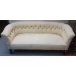Edwardian cream ground upholstered button back double ended sofa on mahogany supports and casters.