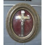 Plated metal crucifix within oval gilded frame having convex glass. Overall 47 x 39cm approx. (B.P.