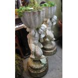 Pair of composite planters having cherub and dolphin mounts standing on a circular stepped base.