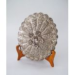 A Persian or Iraqi silver oval mirror with repousse floral decoration on a wooden stand.