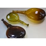 A group of three glass saddle flasks, two brown, the third, smaller, in green each with trailed