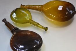 A group of three glass saddle flasks, two brown, the third, smaller, in green each with trailed