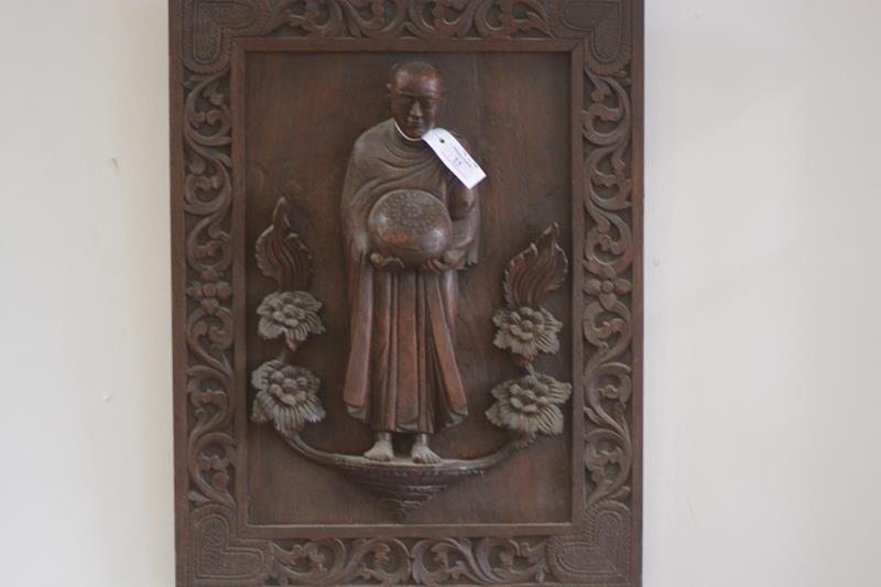 A carved wooden panel of a buddhist monk, in high relief, depicted standing, holding an alms bowl