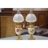 A pair of Edwardian gilt-brass mounted blush ivory porcelain oil lamps, each vase painted with
