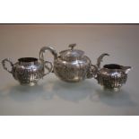 An Oriental white metal three piece tea service, c. 1900, each piece chased with panels of bamboo,