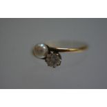 A diamond and pearl two stone ring, the round brilliant-cut stone claw-set in a crossover mount on a