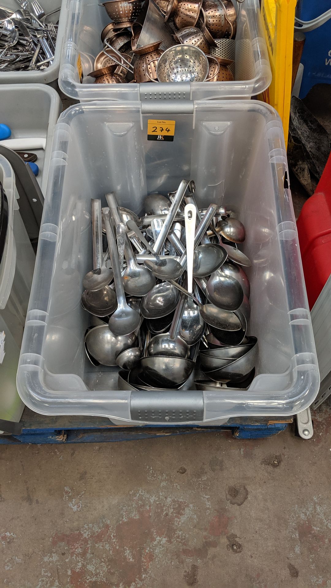 The contents of a crate of large commercial catering utensils, particularly spoons & ladles