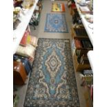 Two blue patterned rugs, a small mat with camels and riders and a rug pinned to a board