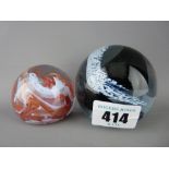 Two paperweights, one swirling cloud and snow and the other orange and white waves