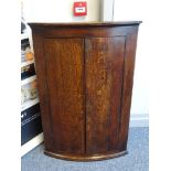 AN ANTIQUE OAK BOW FRONT TWO DOOR HANGING CORNER CUPBOARD, the doors with diamond shaped escutcheon,