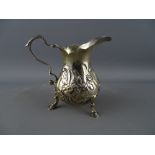 A GEORGE III SILVER CREAM JUG with floral embossed body and scroll handle on three hoof feet, London