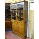 A SLIM GOLDEN OAK BOOKCASE CUPBOARD having twin upper glazed panel doors and base cupboard doors