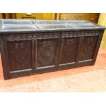 AN ANTIQUE BLACKENED OAK LIDDED PANELLED COFFER, having carved front detail, 68 cms high, 152 cms