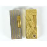 Two Dunhill gas cigarette lighters - a bark textured gold plated example and a white metal version
