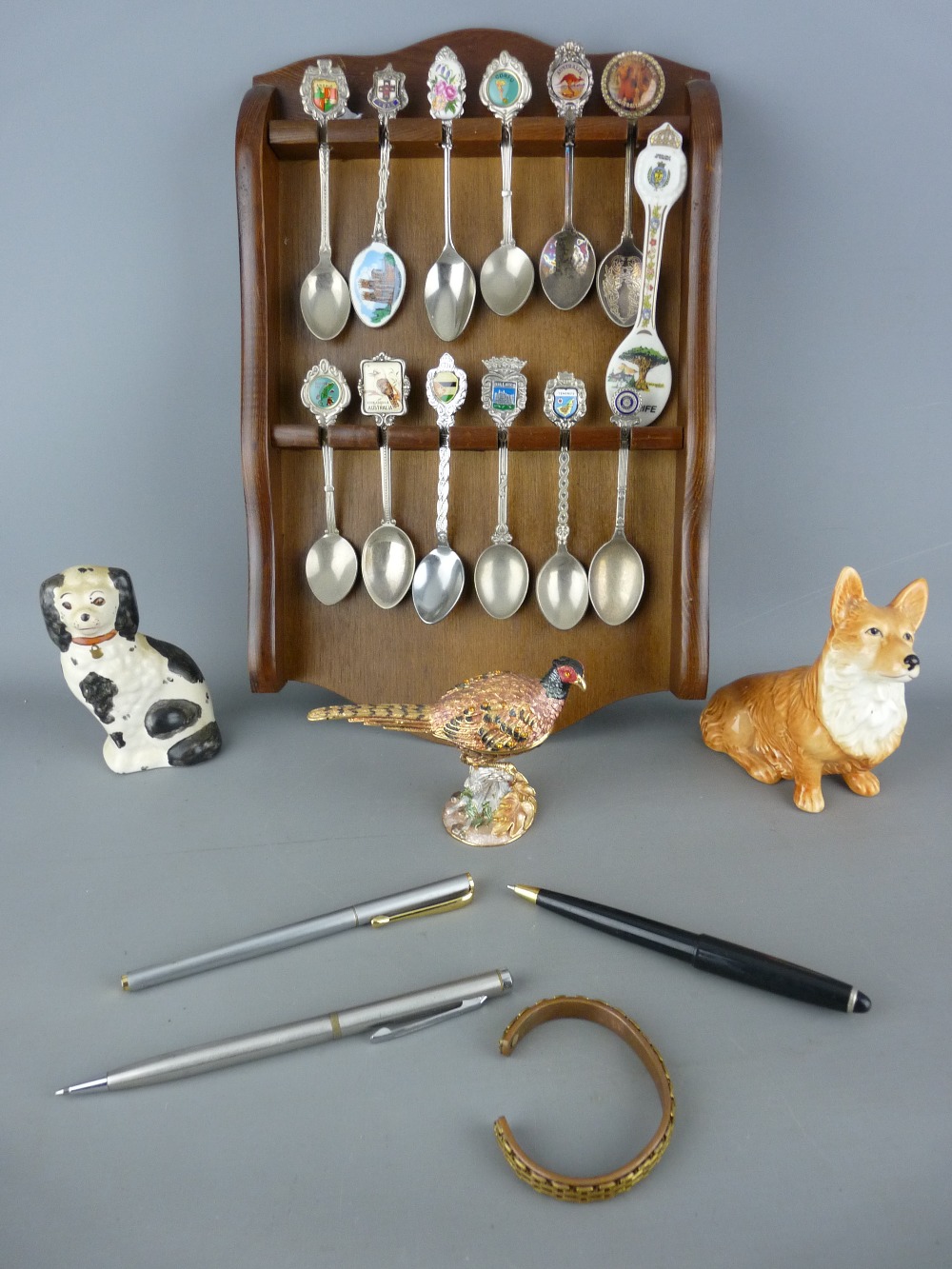 Quantity of collector's spoons on a wooden rack, a Sylvac corgi and a Staffs comforter dog, a gilt