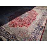 A large Persian Kashan rug with red centre decoration and blue and gold border, 410 x 292cms (A/F)