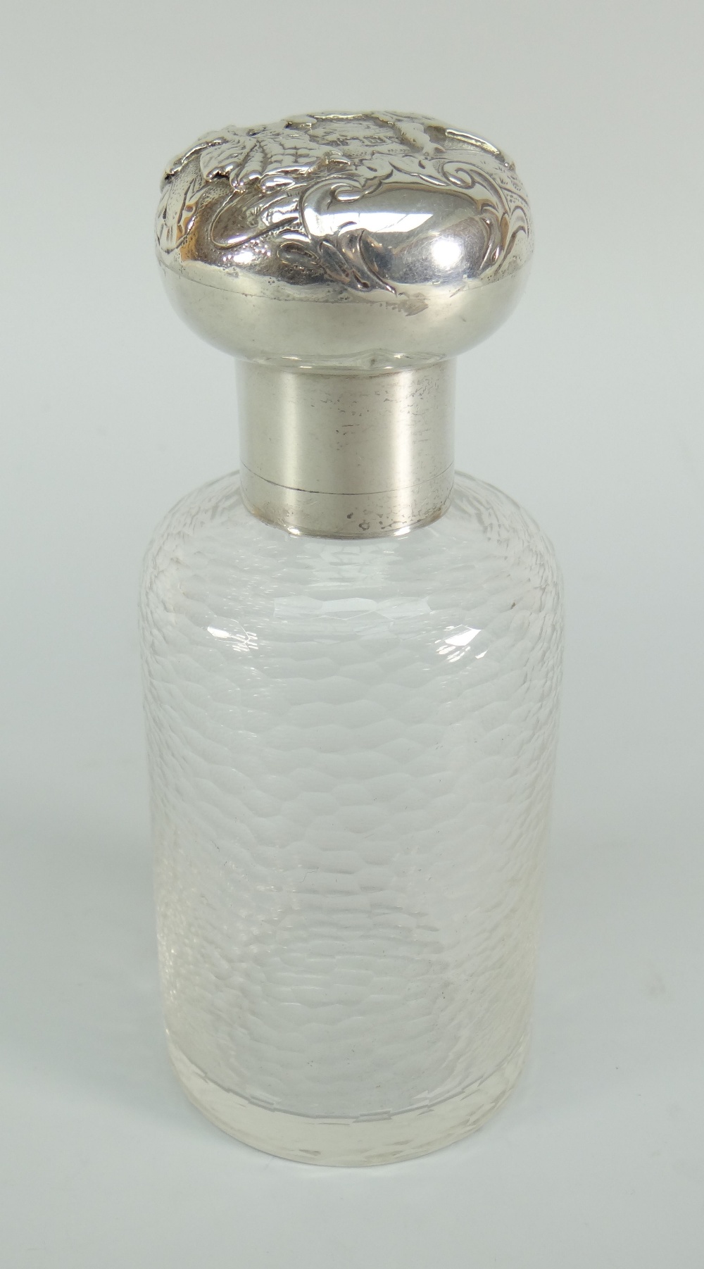 A textured glass dressing table bottle with silver screw lid and collar having repousse decoration