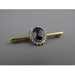 A NEAT SHORT NINE CARAT GOLD BAR BROOCH with large oval dark sapphire and surrounding small