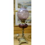 An antique cherubic brass oil lamp on four scroll feet and with dimpled purple glass reservoir and