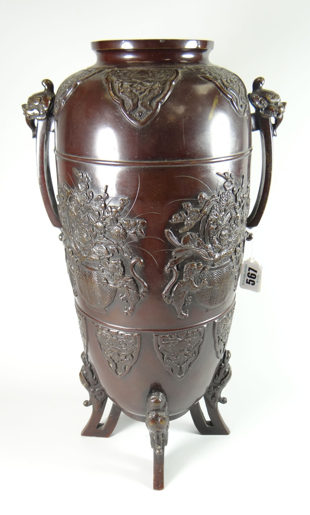 A tall bronze Chinese temple vase of ovoid form on four dragon feet and with beast-mask terminals to